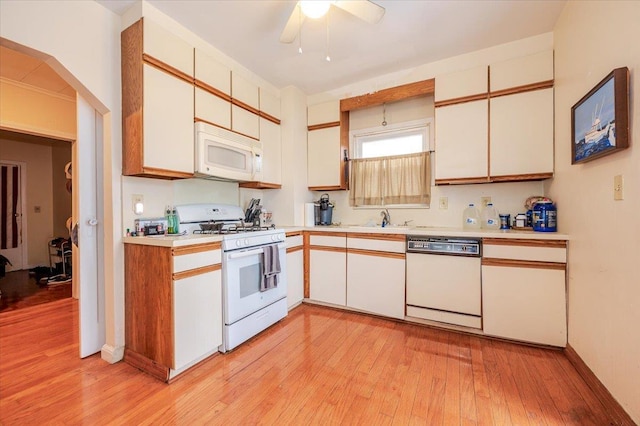 kitchen with light countertops, light wood-style floors, white cabinets, white appliances, and a sink