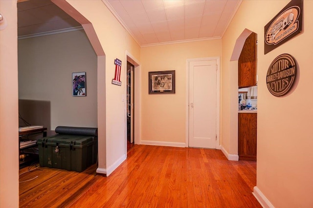 hallway featuring arched walkways, light wood-type flooring, crown molding, and baseboards