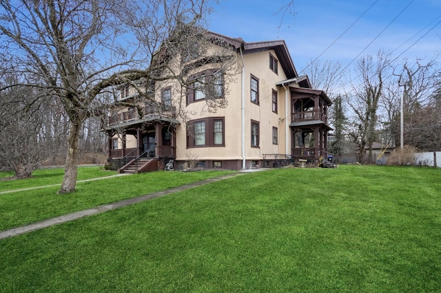 rear view of property with stucco siding, a balcony, and a lawn