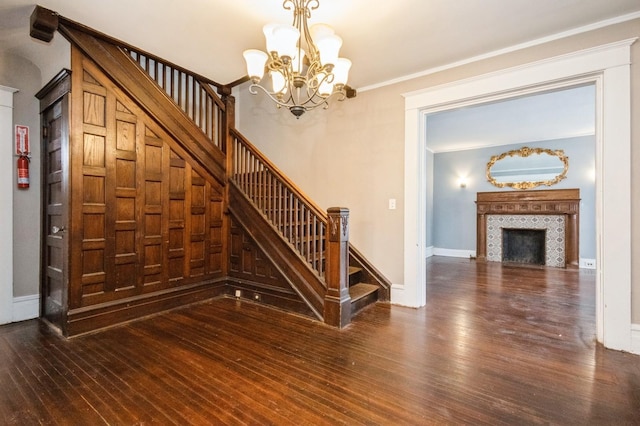 staircase featuring ornamental molding, a tiled fireplace, hardwood / wood-style flooring, an inviting chandelier, and baseboards