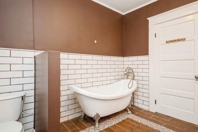 bathroom featuring a soaking tub, toilet, wood finish floors, and a wainscoted wall