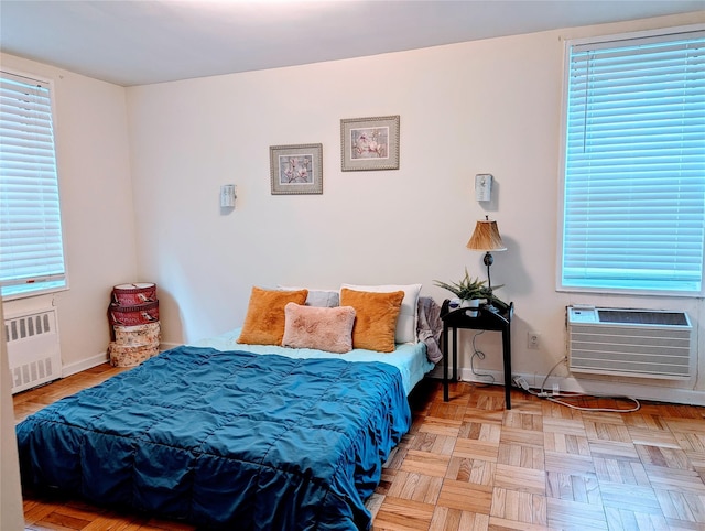 bedroom with an AC wall unit, multiple windows, radiator heating unit, and baseboards