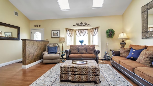 living area with baseboards, lofted ceiling with skylight, visible vents, and wood finished floors