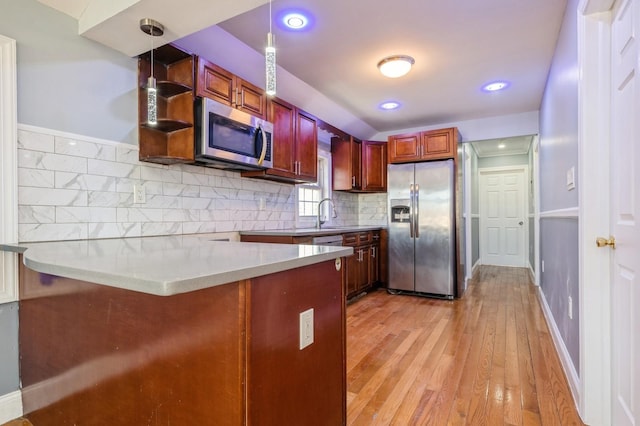 kitchen with tasteful backsplash, decorative light fixtures, light wood-type flooring, a peninsula, and stainless steel appliances