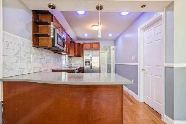 kitchen featuring light wood finished floors, light countertops, a peninsula, stainless steel appliances, and a sink