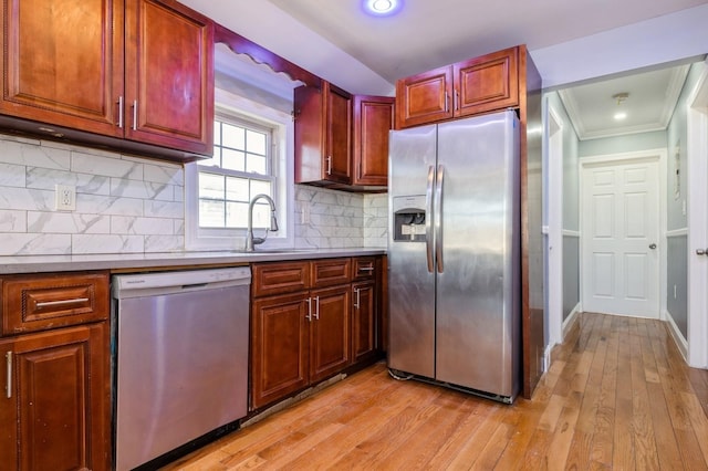 kitchen featuring a sink, decorative backsplash, ornamental molding, stainless steel appliances, and light wood-type flooring