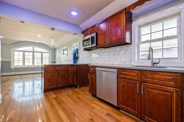 kitchen with tasteful backsplash, a peninsula, light wood-style floors, stainless steel appliances, and a sink