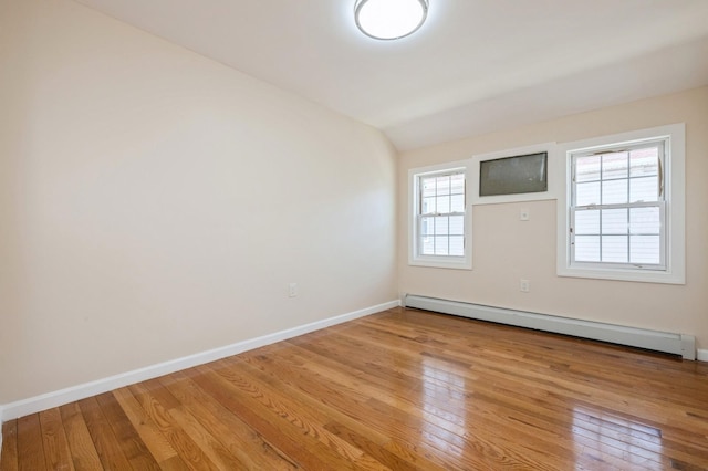 empty room featuring light wood-style floors, baseboards, baseboard heating, and vaulted ceiling