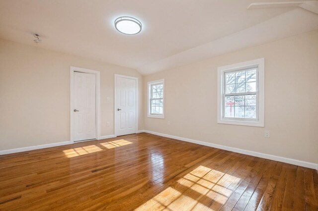 spare room featuring lofted ceiling, baseboards, and wood-type flooring