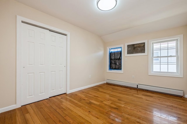 unfurnished bedroom featuring light wood-type flooring, a baseboard heating unit, baseboards, and vaulted ceiling