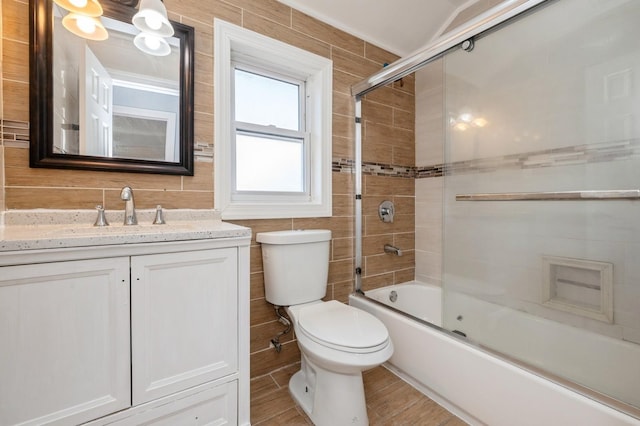 full bath featuring vanity, wood finished floors, bath / shower combo with glass door, tile walls, and toilet