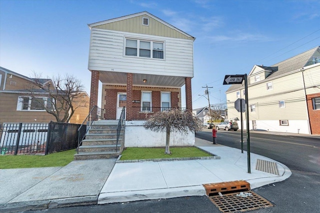 view of front of house with brick siding, covered porch, and fence