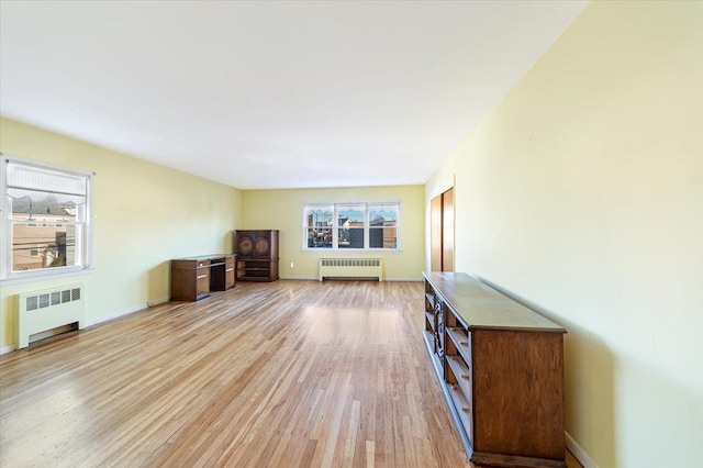 unfurnished living room with light wood finished floors, a healthy amount of sunlight, and radiator heating unit