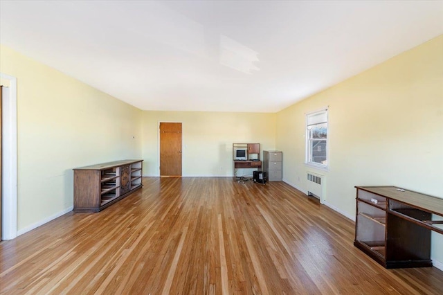 unfurnished living room with radiator heating unit, wood finished floors, and baseboards