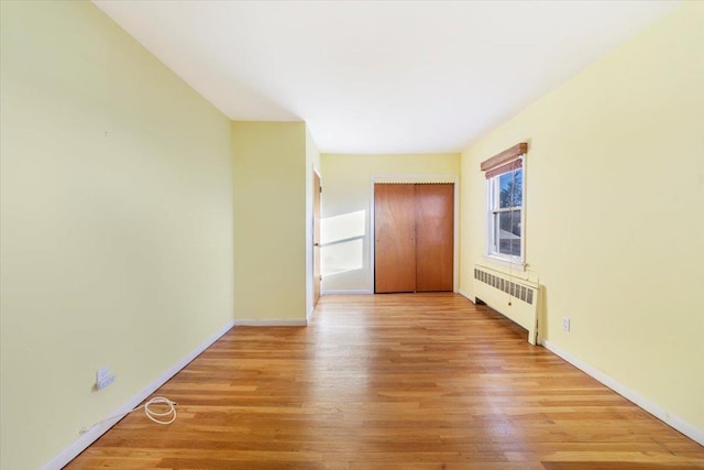 empty room featuring light wood-type flooring, baseboards, and radiator heating unit