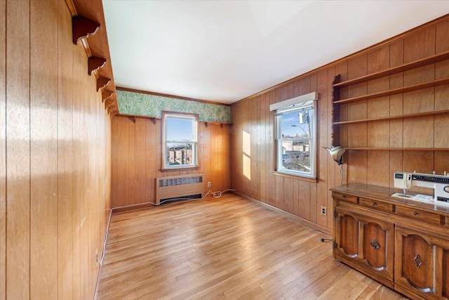 unfurnished office featuring light wood-type flooring, baseboards, radiator, and wooden walls