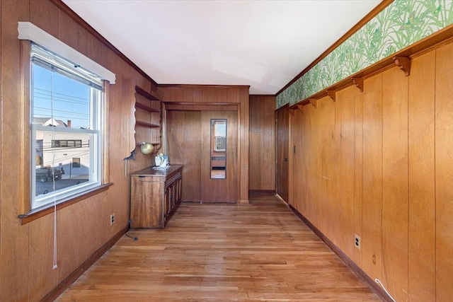 doorway to outside featuring light wood-style flooring, wood walls, baseboards, and ornamental molding