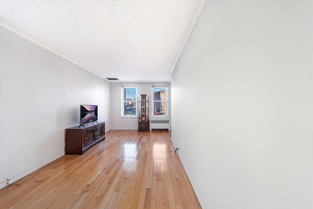 unfurnished living room with visible vents, radiator, crown molding, light wood finished floors, and baseboards