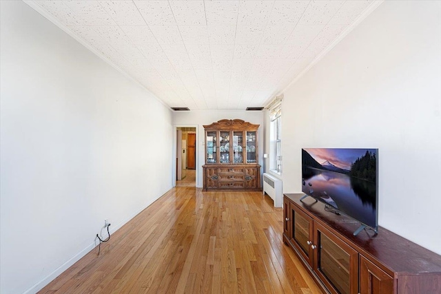 unfurnished living room featuring radiator, light wood-style flooring, and ornamental molding