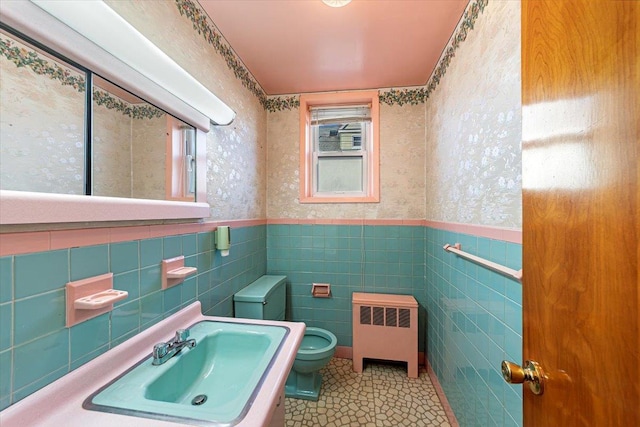 bathroom with wallpapered walls, toilet, radiator heating unit, wainscoting, and a sink