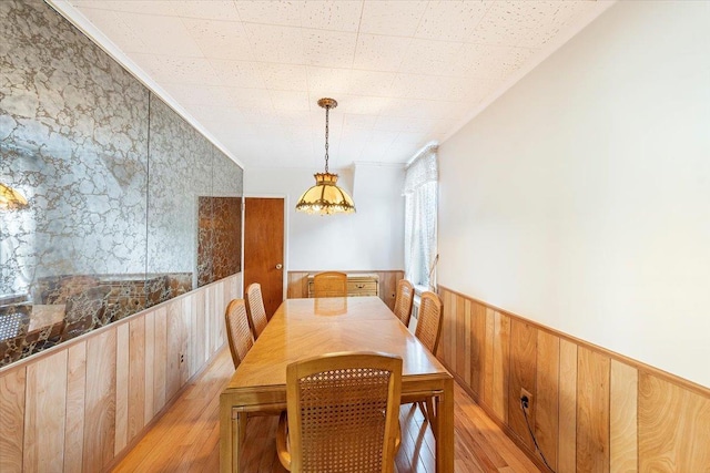 dining space with crown molding, wooden walls, light wood-style floors, and a wainscoted wall