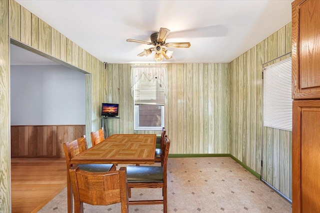 dining space with baseboards, light floors, ceiling fan, and wooden walls