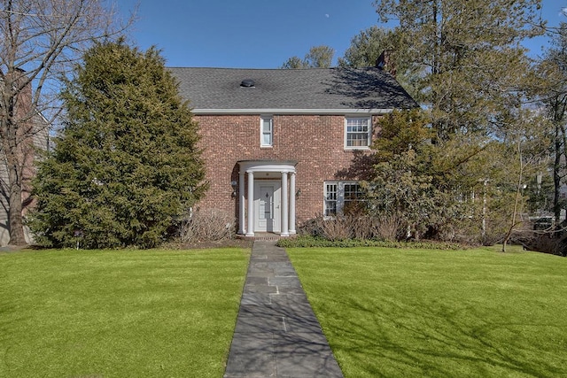 colonial house with brick siding, a front lawn, and a shingled roof