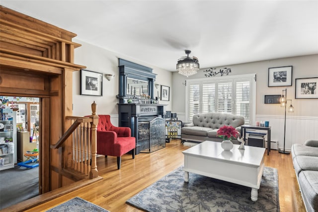 living area featuring a fireplace, light wood-style floors, wainscoting, a baseboard heating unit, and a chandelier