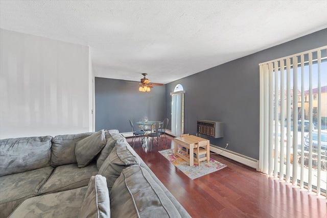 living room with a ceiling fan, a textured ceiling, wood finished floors, a wall unit AC, and baseboard heating