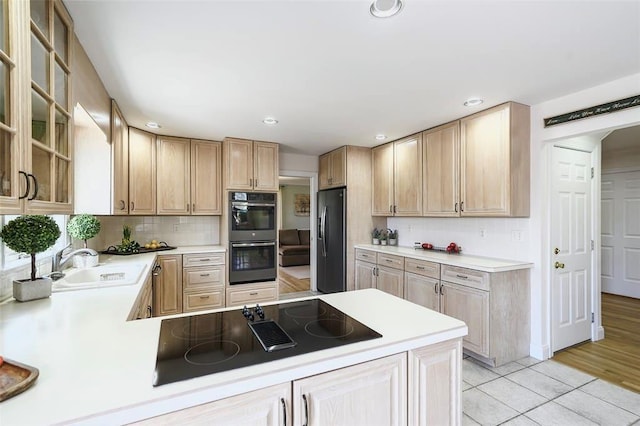 kitchen with fridge with ice dispenser, black electric cooktop, a sink, multiple ovens, and light countertops