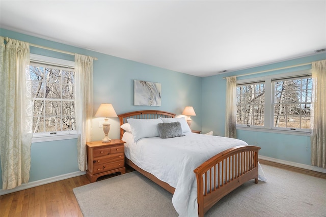 bedroom featuring visible vents, baseboards, multiple windows, and hardwood / wood-style flooring