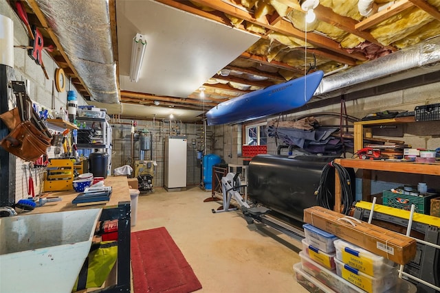 unfinished below grade area featuring water heater, freestanding refrigerator, and heating fuel