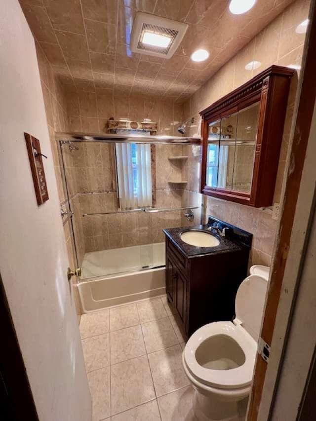 bathroom featuring visible vents, tile walls, toilet, combined bath / shower with glass door, and tile patterned floors