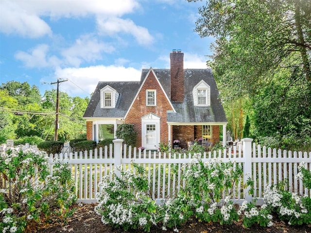 new england style home featuring a fenced front yard, a high end roof, brick siding, and a chimney