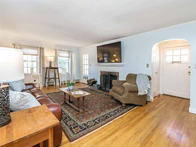 living area with hardwood / wood-style floors, baseboards, a fireplace, arched walkways, and crown molding