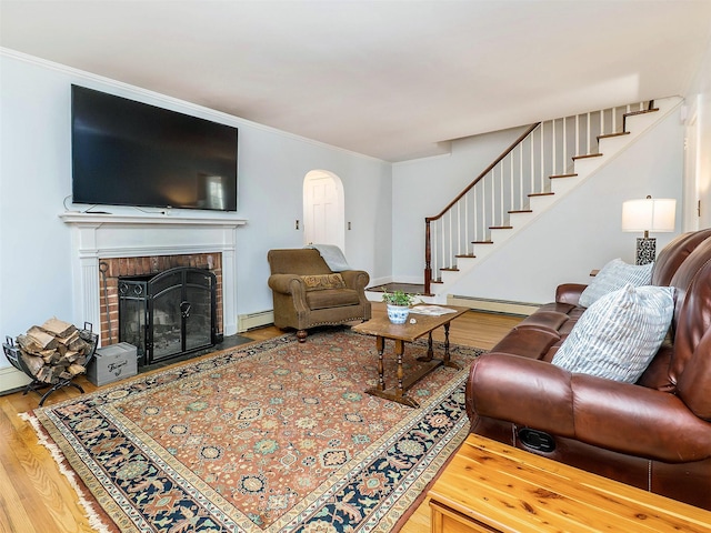 living room featuring a brick fireplace, stairs, a baseboard heating unit, and wood finished floors