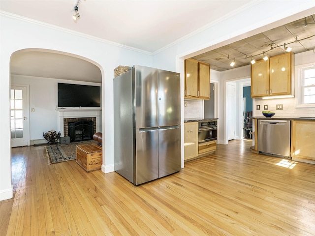 kitchen featuring tasteful backsplash, crown molding, light wood-type flooring, appliances with stainless steel finishes, and a fireplace