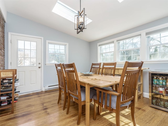 dining area with light wood finished floors, lofted ceiling with skylight, beverage cooler, an inviting chandelier, and a baseboard radiator