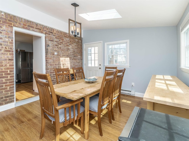 dining space with lofted ceiling with skylight, light wood-style flooring, brick wall, and a baseboard radiator