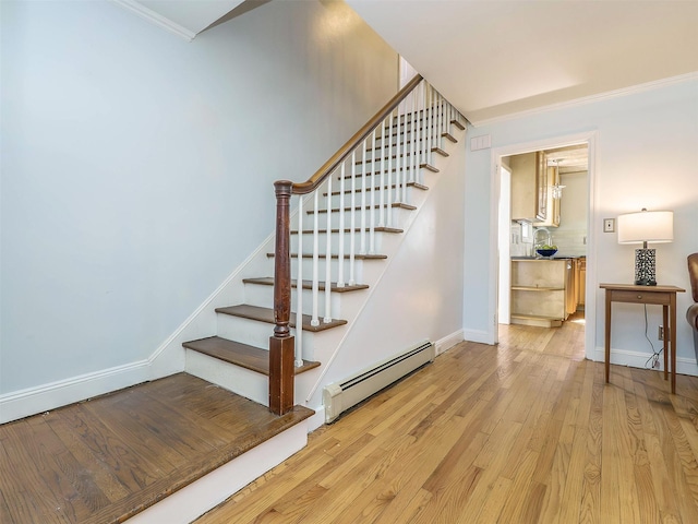 stairway with baseboards, baseboard heating, wood finished floors, and crown molding