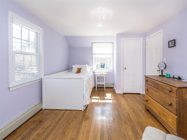 bedroom featuring a baseboard radiator, multiple windows, light wood-style floors, and baseboards