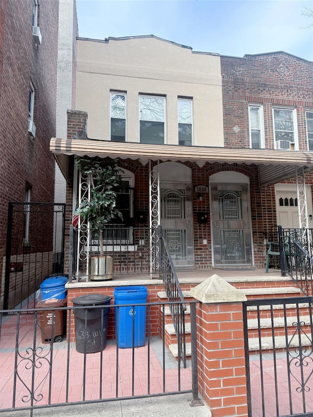 townhome / multi-family property featuring brick siding, covered porch, a fenced front yard, and stucco siding