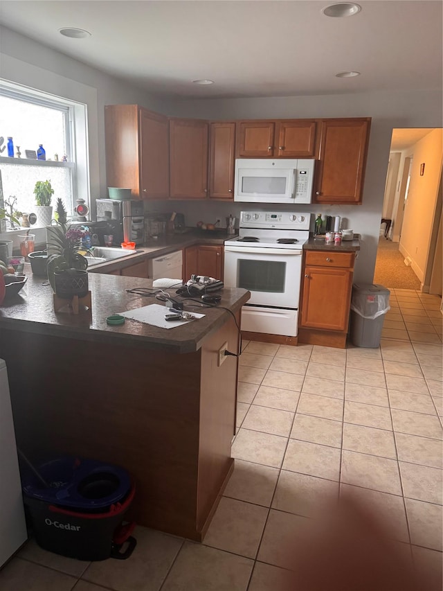 kitchen with white appliances, light tile patterned floors, dark countertops, and a peninsula