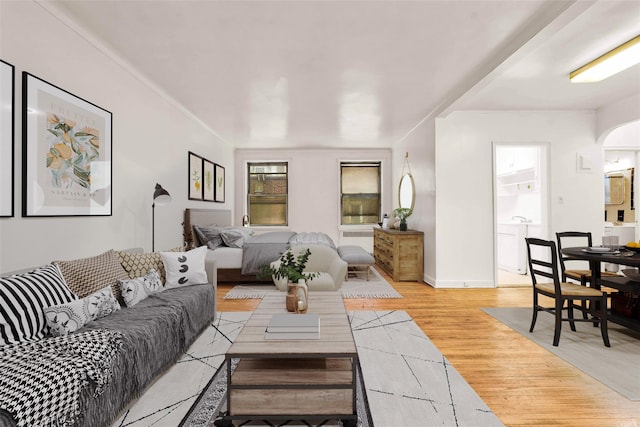 living area with baseboards, arched walkways, and light wood finished floors