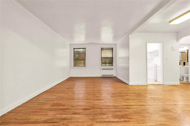 unfurnished living room featuring wood finished floors, radiator heating unit, arched walkways, baseboards, and washer / dryer