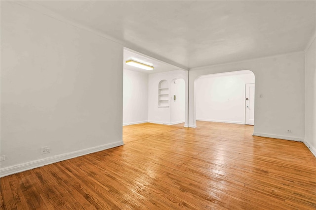 spare room featuring baseboards, built in shelves, arched walkways, and light wood finished floors