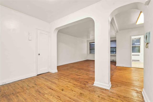 spare room featuring radiator heating unit, light wood-style floors, arched walkways, and baseboards