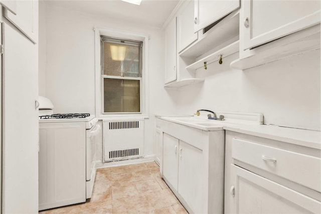 kitchen with radiator, a sink, light countertops, white cabinetry, and white gas range