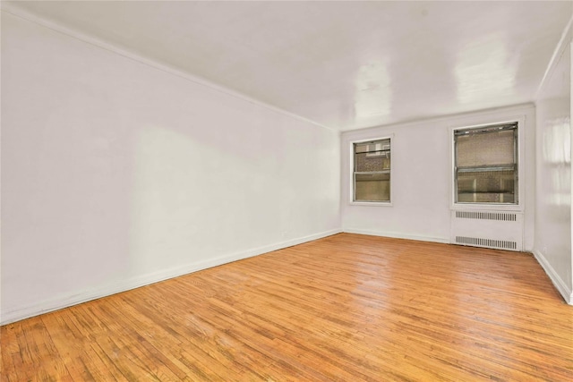 empty room with light wood-style floors, baseboards, and radiator