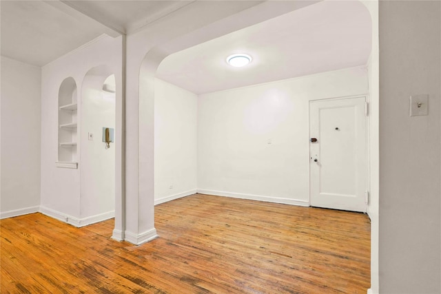 spare room with built in shelves, wood finished floors, and baseboards